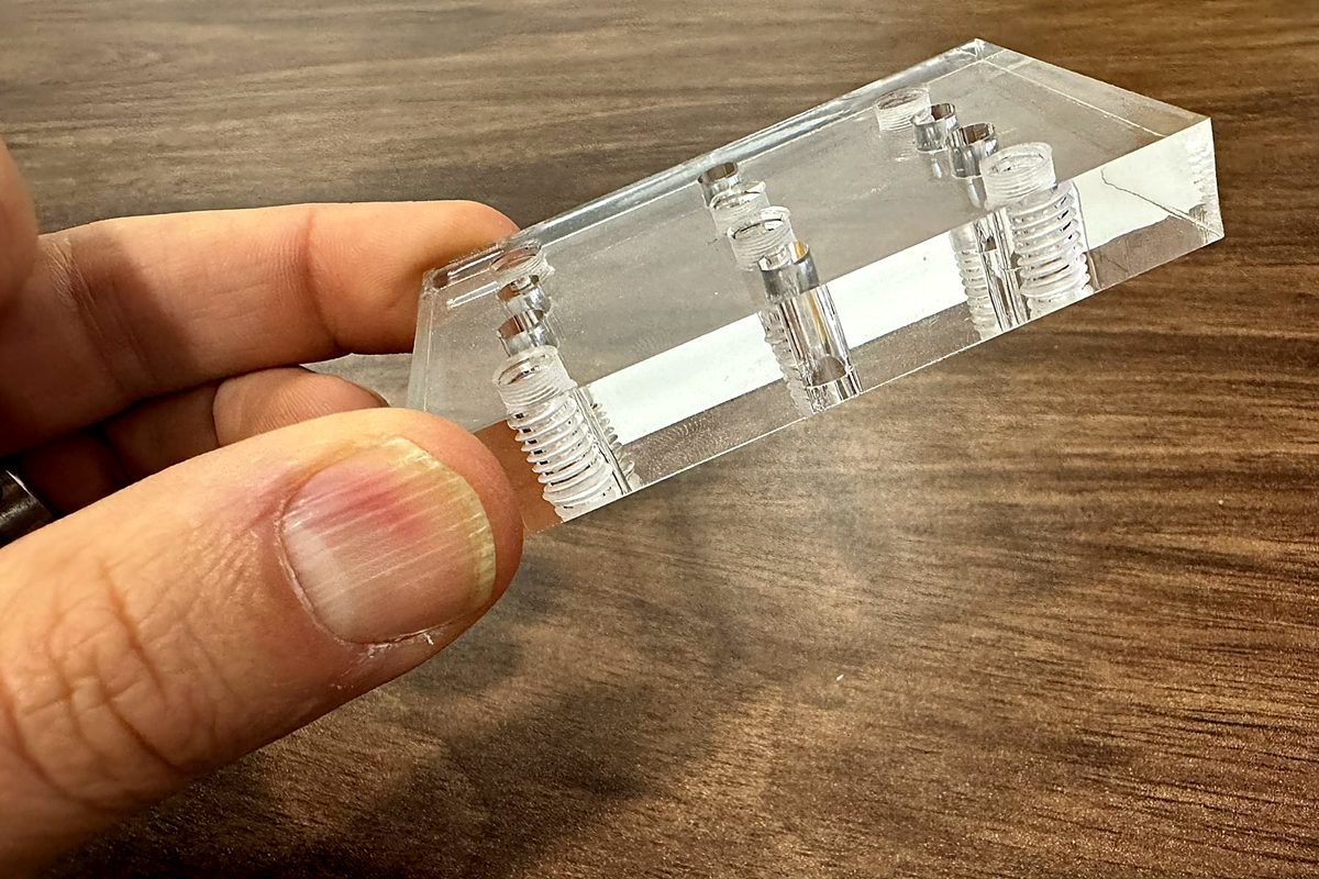 Clear acrylic part with tapped holes held up for inspection at ACP Waterjet
