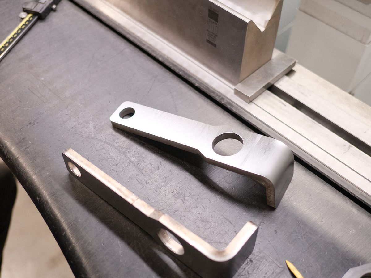Two bent steel brackets with drilled holes on the press brake bed at ACP Waterjet