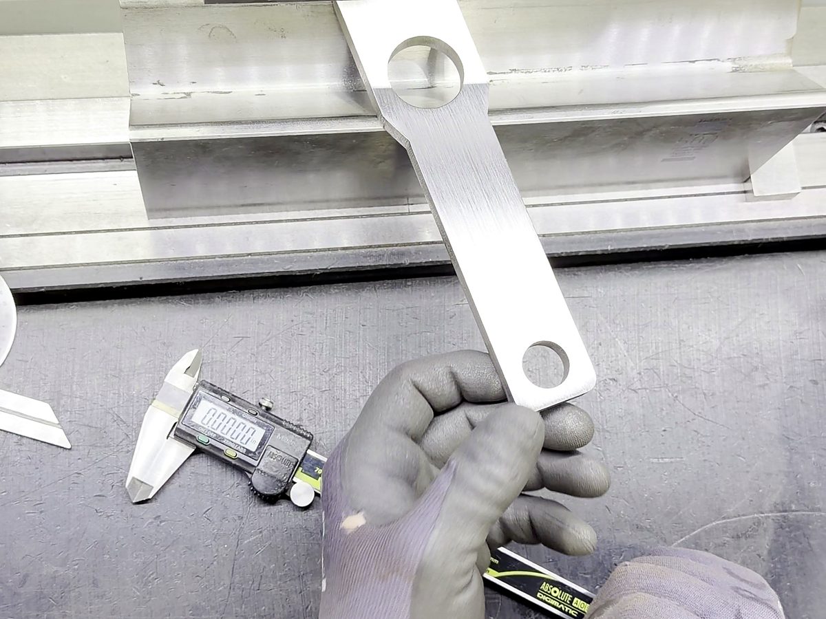 Gloved hands hold a bent bracket and a caliper for a measurement at ACP Waterjet