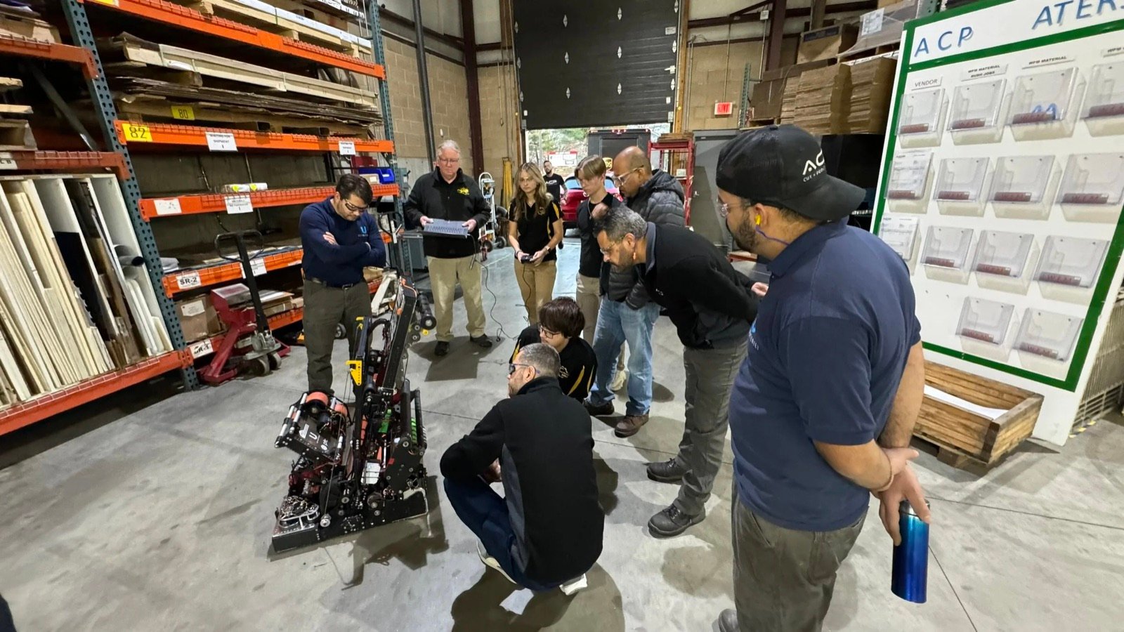 ACP staff and a visiting student robotics team gathered around a competition robot in the ACP warehouse