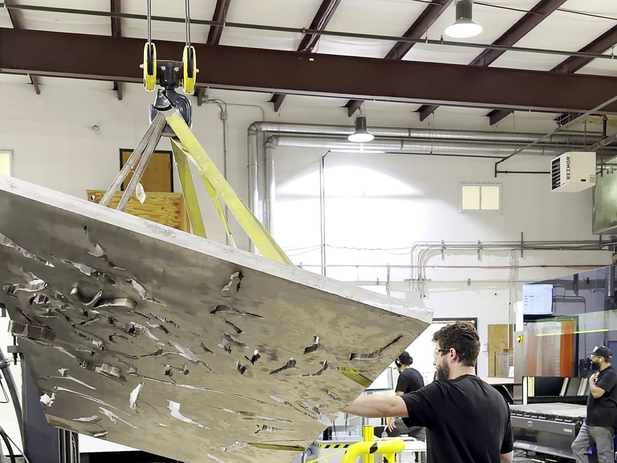 A waterjet cut plate skeleton carried across the ACP shop floor by the overhead crane