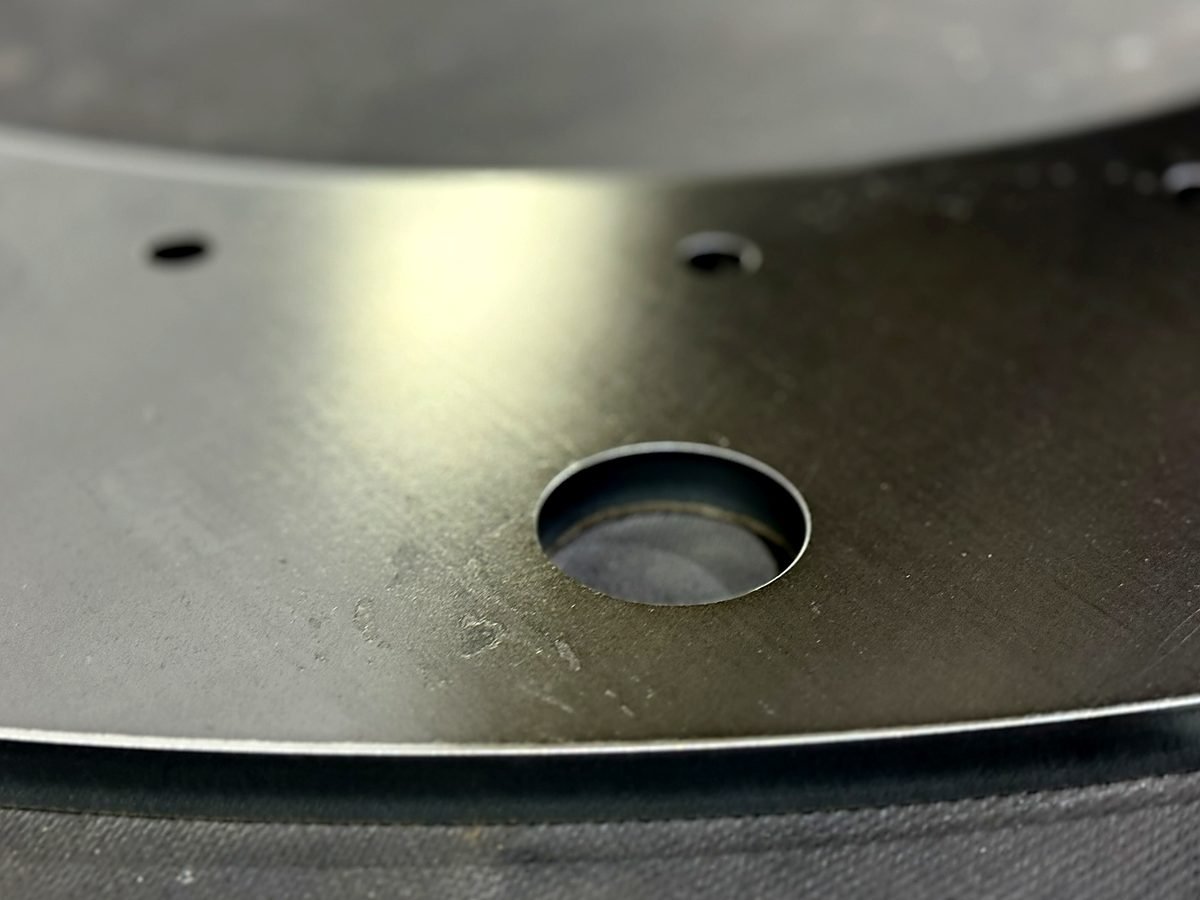 Close up of a smooth deburred edge and countersunk hole on a steel plate at ACP Waterjet