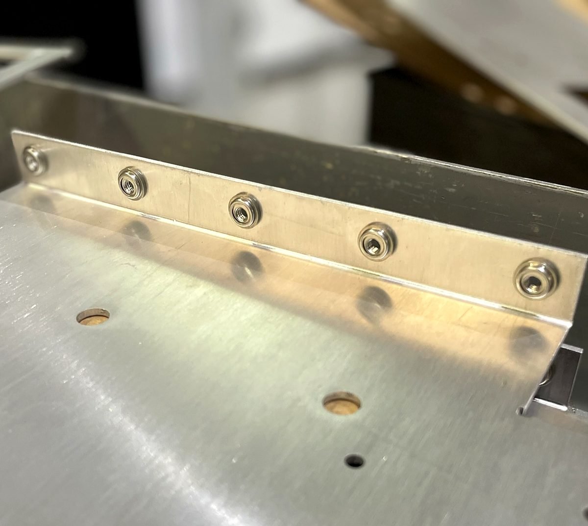 Close up of press in hardware installed along a bent aluminum panel at ACP Waterjet