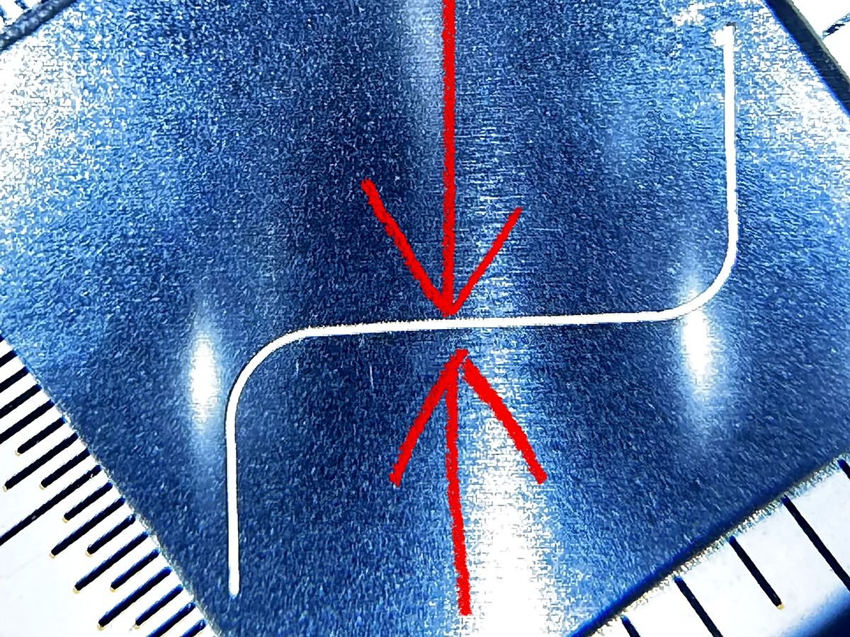 Curved laser cut kerf line seen through a measuring loupe, arrows marking the cut width