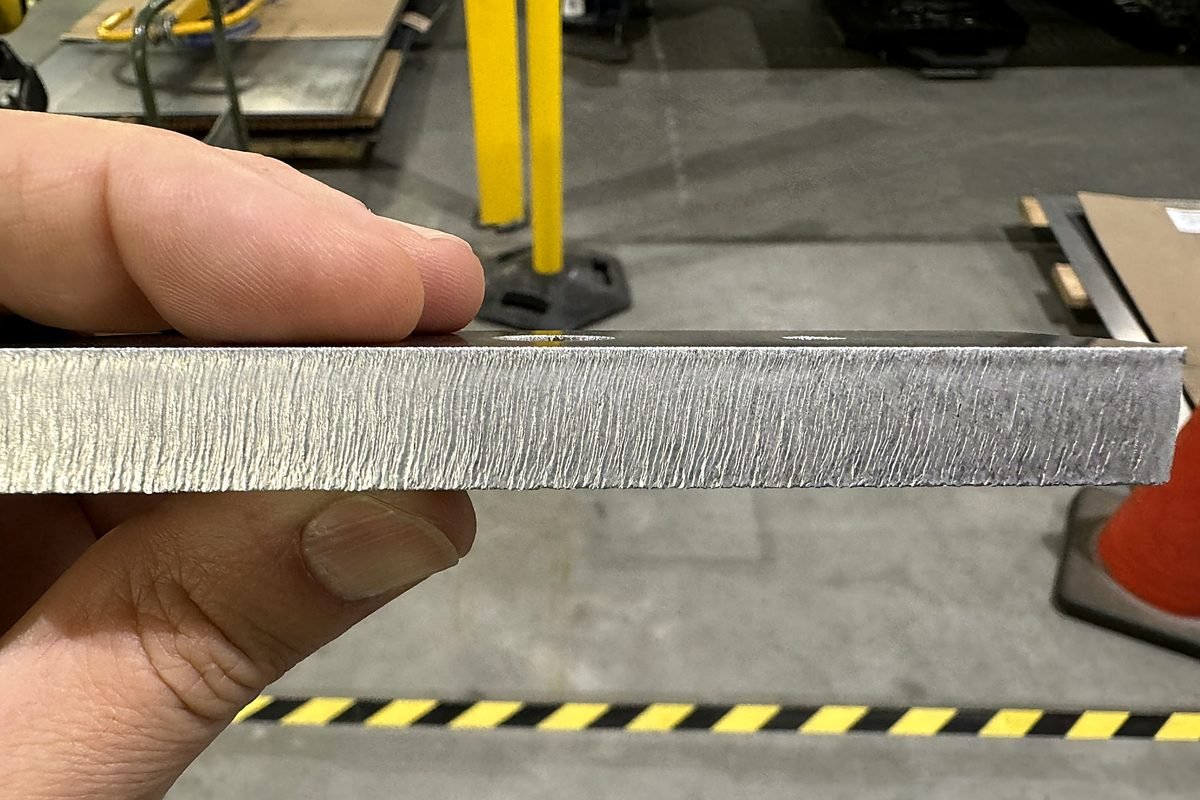 Hand holding a laser cut plate edge showing material thickness and finish at ACP Waterjet