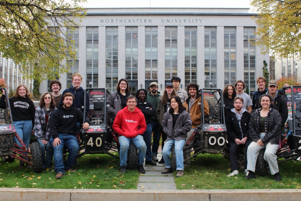 The Northeastern Baja SAE team on the lawn between two of its off-road cars
