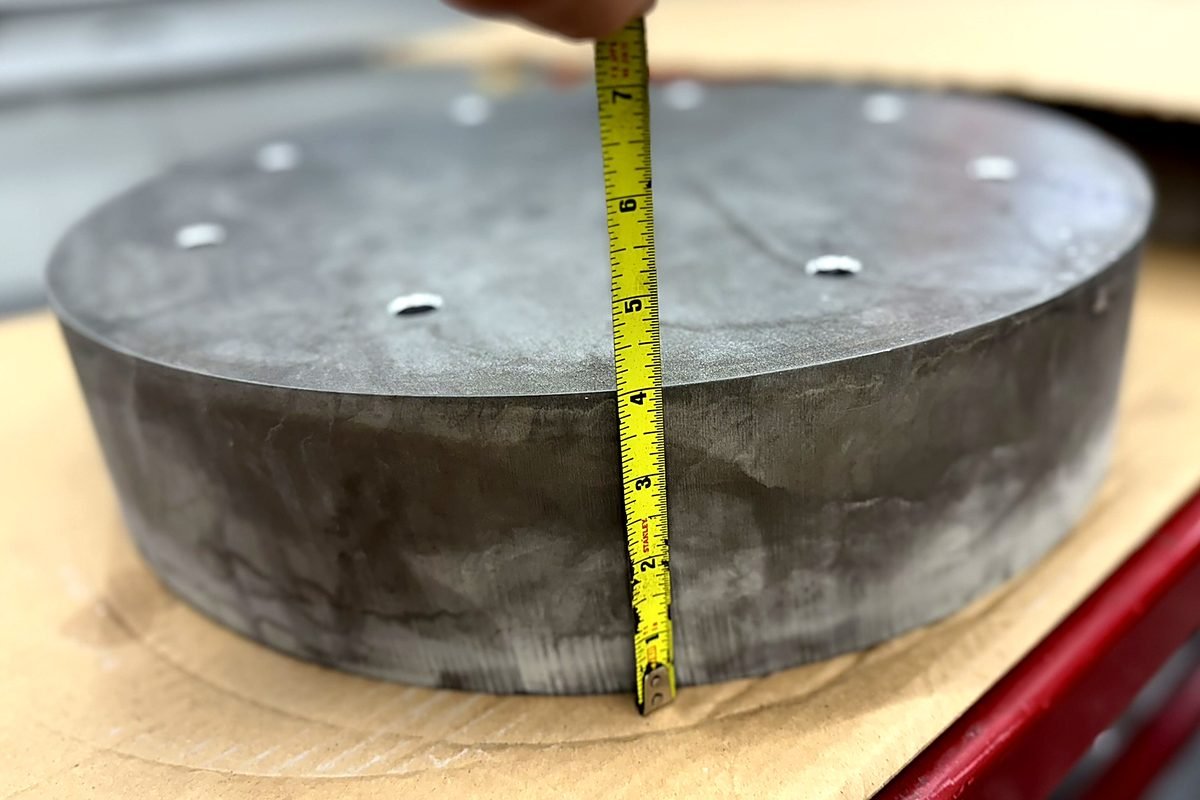 Tape measure showing a 4 inch thick waterjet cut aluminum disc at ACP Waterjet in Littleton, MA