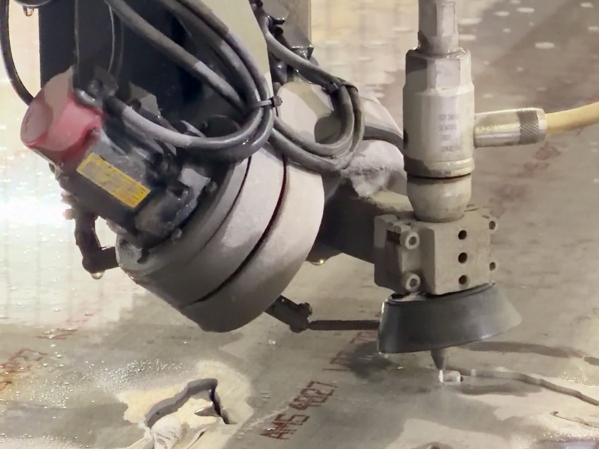 Abrasive waterjet cutting head over a wet steel plate with a fresh cut slot below the nozzle, at ACP Waterjet in Littleton, MA