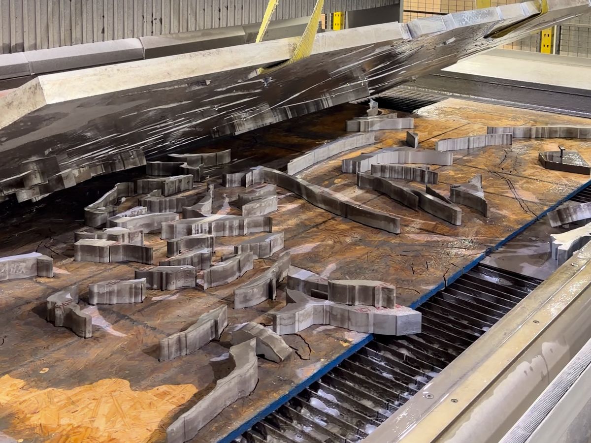 Cut steel parts covered in garnet on the waterjet table grating as the cut plate is lifted away, at ACP Waterjet
