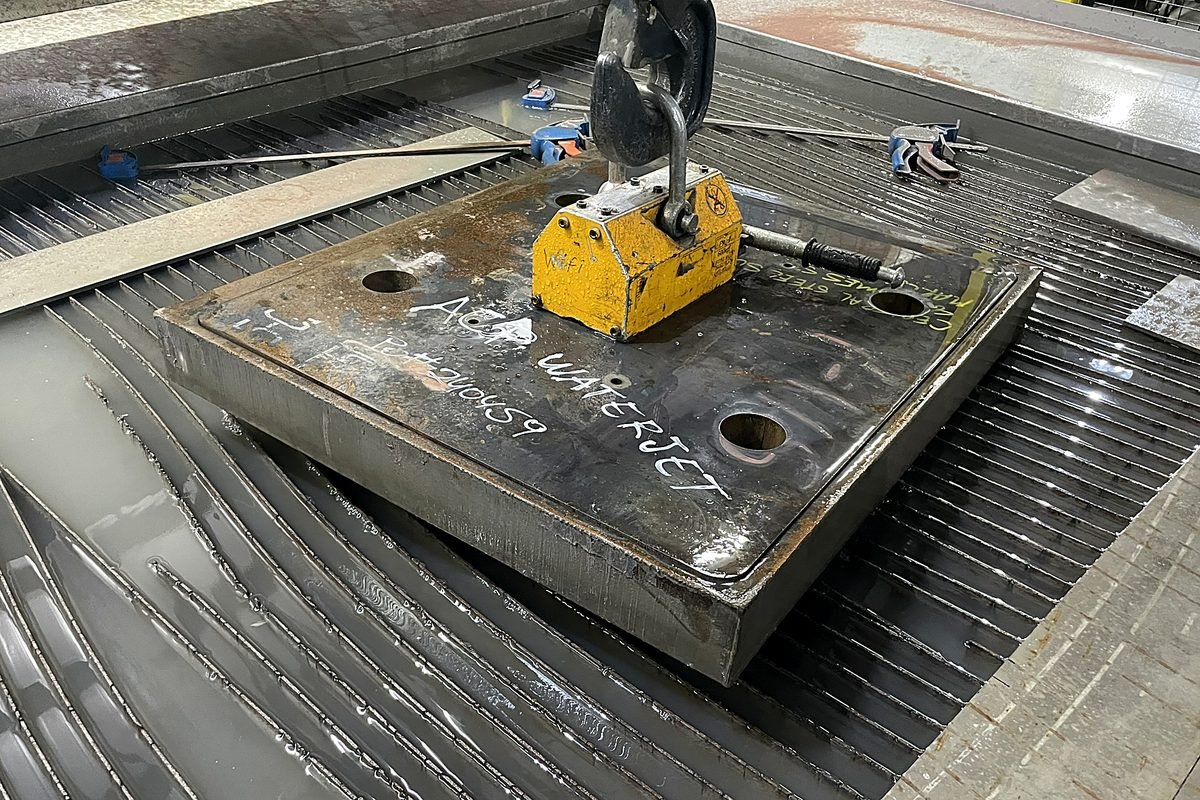 Lifting magnet moving a thick steel plate off the waterjet cutting bed at ACP Waterjet